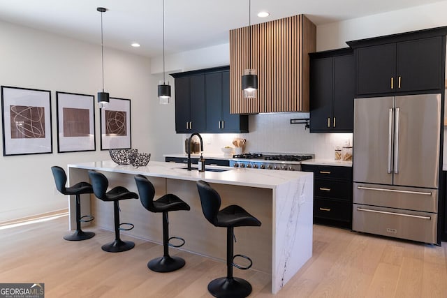 kitchen with sink, decorative light fixtures, light hardwood / wood-style flooring, an island with sink, and stainless steel appliances