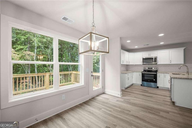 kitchen featuring pendant lighting, sink, decorative backsplash, white cabinetry, and stainless steel appliances