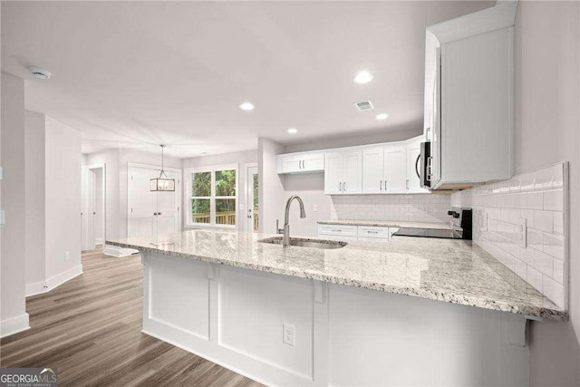 kitchen featuring backsplash, range, kitchen peninsula, sink, and white cabinetry