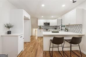 kitchen with a kitchen bar, kitchen peninsula, white cabinets, and light hardwood / wood-style floors