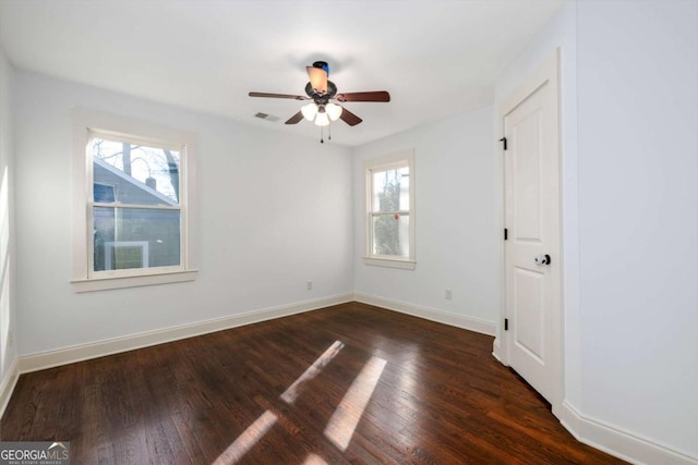 empty room featuring a wealth of natural light, ceiling fan, and dark hardwood / wood-style floors