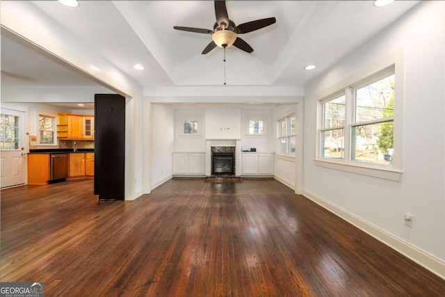 unfurnished living room featuring a fireplace, a raised ceiling, ceiling fan, and dark wood-type flooring