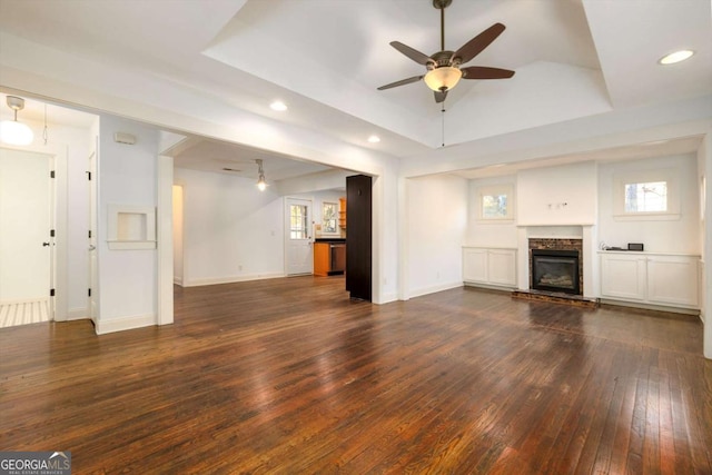 unfurnished living room featuring a raised ceiling, dark hardwood / wood-style flooring, ceiling fan, and a stone fireplace