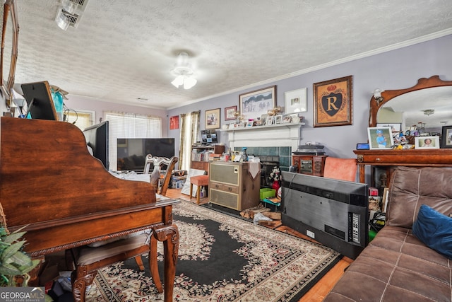 living room with crown molding, wood-type flooring, a textured ceiling, and a tile fireplace