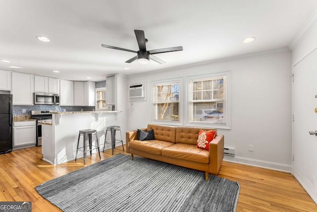 living room featuring light wood-type flooring, ceiling fan, ornamental molding, and a wall mounted AC