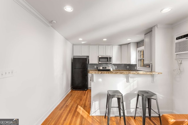 kitchen featuring kitchen peninsula, stainless steel appliances, tasteful backsplash, a kitchen breakfast bar, and white cabinets