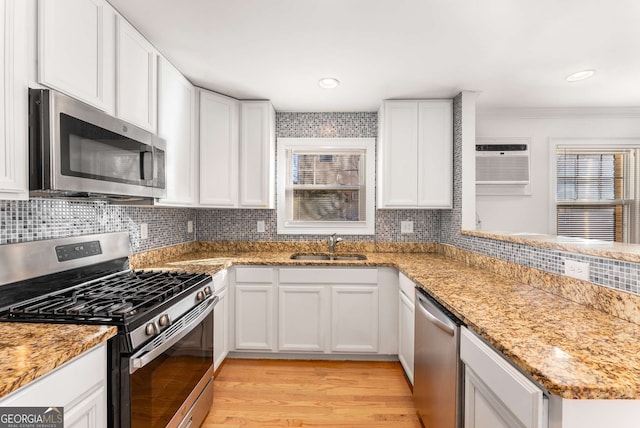 kitchen with white cabinets, appliances with stainless steel finishes, light hardwood / wood-style floors, sink, and light stone counters