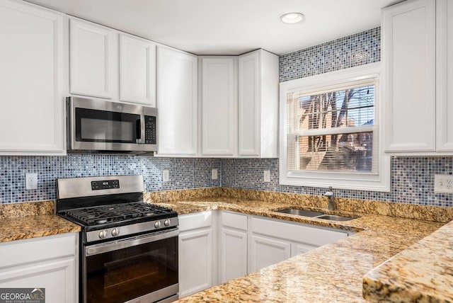 kitchen with appliances with stainless steel finishes, white cabinetry, light stone counters, and sink