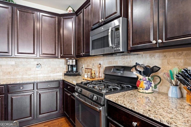 kitchen featuring dark brown cabinetry, stainless steel appliances, light stone counters, and backsplash