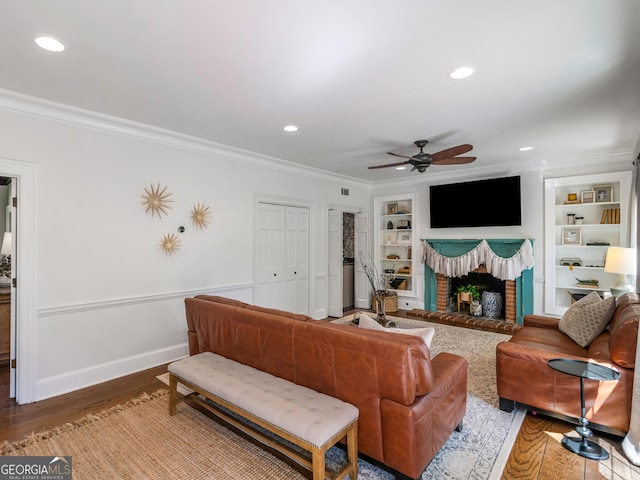 living room with built in shelves, crown molding, ceiling fan, and hardwood / wood-style flooring