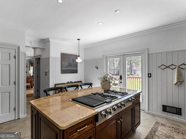 kitchen featuring a center island, stainless steel gas cooktop, light stone counters, pendant lighting, and ornamental molding