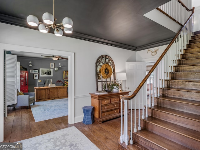 stairs with wood-type flooring, ceiling fan with notable chandelier, and ornamental molding