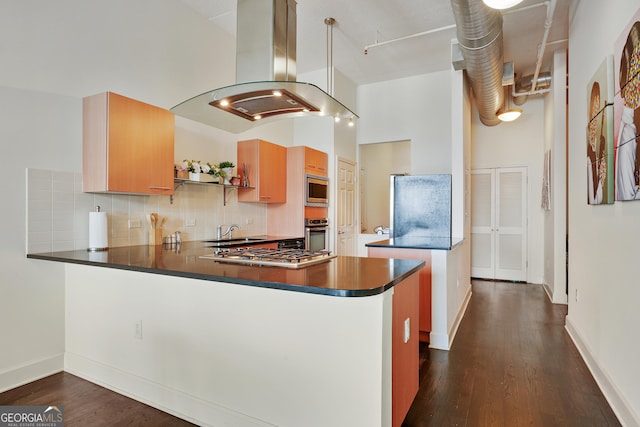 kitchen featuring dark wood-type flooring, decorative backsplash, appliances with stainless steel finishes, island range hood, and kitchen peninsula