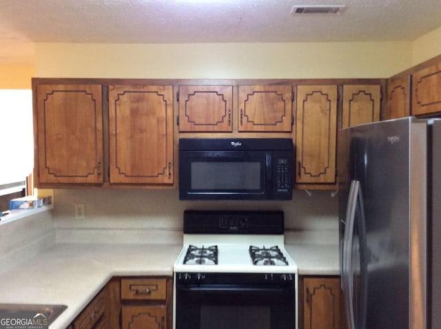 kitchen with white gas range, stainless steel fridge, and a textured ceiling