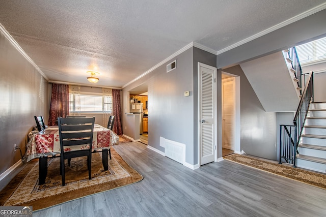 dining room with wood-type flooring, a textured ceiling, and ornamental molding