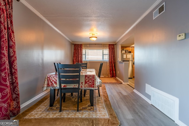 dining area with a textured ceiling, hardwood / wood-style flooring, and crown molding