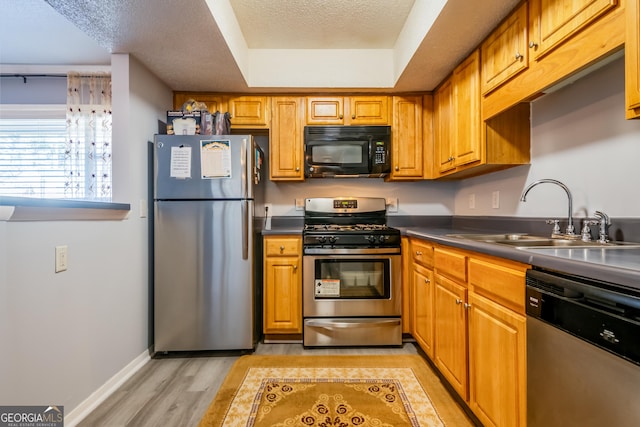 kitchen with appliances with stainless steel finishes, a textured ceiling, light hardwood / wood-style flooring, and sink