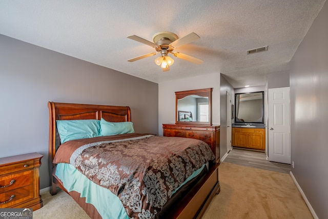 bedroom featuring a textured ceiling, ceiling fan, light carpet, and ensuite bath