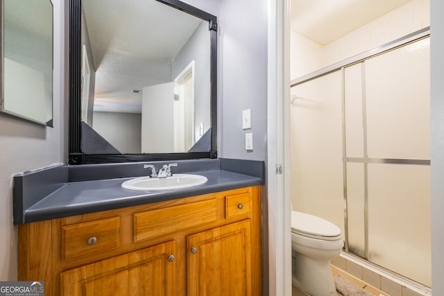 bathroom with a textured ceiling, vanity, toilet, and a shower with shower door