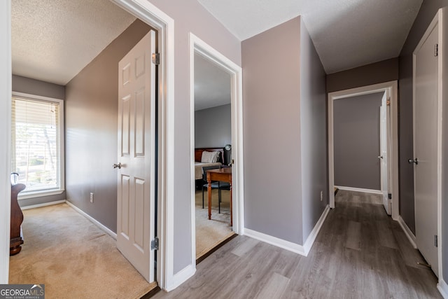 hallway with light hardwood / wood-style floors and a textured ceiling