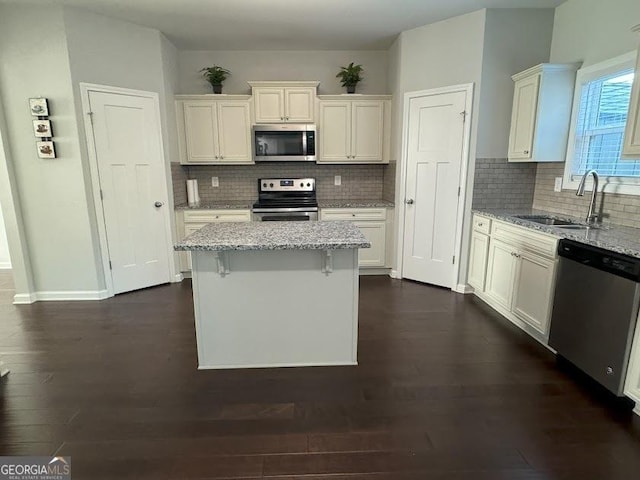 kitchen with sink, a center island, light stone counters, white cabinets, and appliances with stainless steel finishes