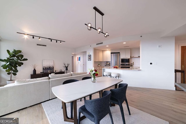 dining room with light wood-type flooring, rail lighting, and an inviting chandelier