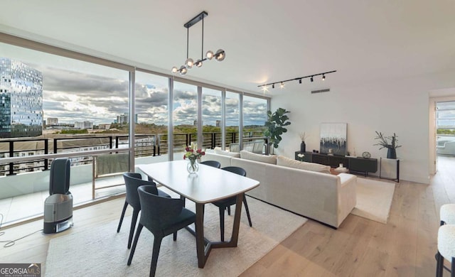 dining area featuring a chandelier, light wood-type flooring, rail lighting, and a wall of windows