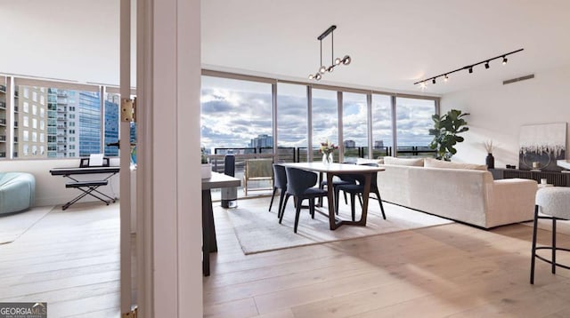 dining area featuring a wall of windows, light wood-type flooring, and rail lighting