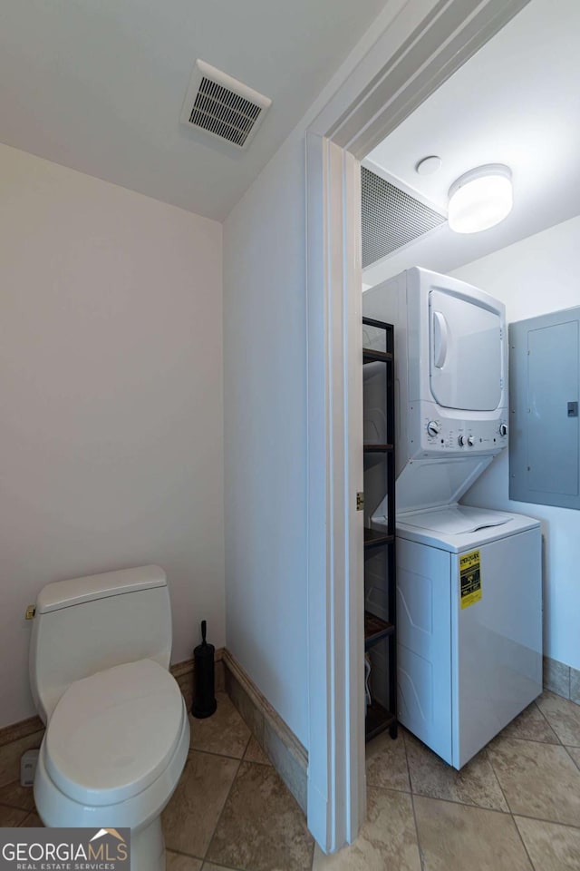 bathroom with tile patterned flooring, toilet, stacked washing maching and dryer, and electric panel