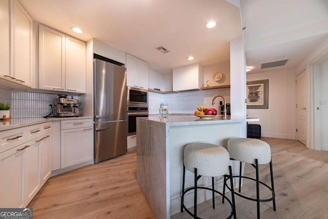 kitchen featuring appliances with stainless steel finishes, light wood-type flooring, tasteful backsplash, and white cabinetry