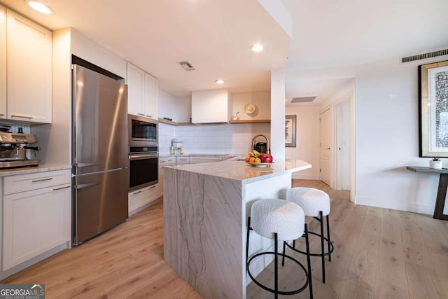 kitchen with backsplash, light hardwood / wood-style floors, a breakfast bar, white cabinets, and appliances with stainless steel finishes