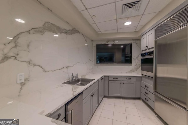 kitchen with gray cabinetry, a drop ceiling, sink, appliances with stainless steel finishes, and light tile patterned flooring