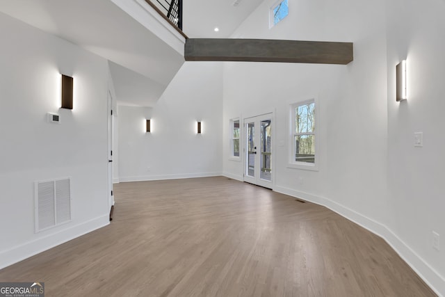 unfurnished living room featuring beam ceiling, high vaulted ceiling, and light wood-type flooring