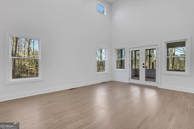 interior space featuring french doors, a towering ceiling, wood-type flooring, and a healthy amount of sunlight