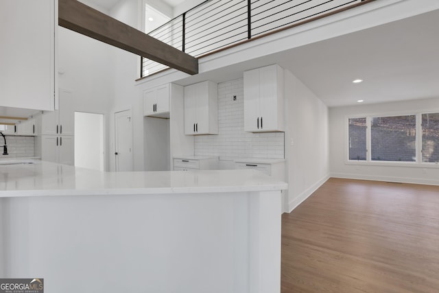 kitchen featuring sink, backsplash, kitchen peninsula, a towering ceiling, and white cabinets