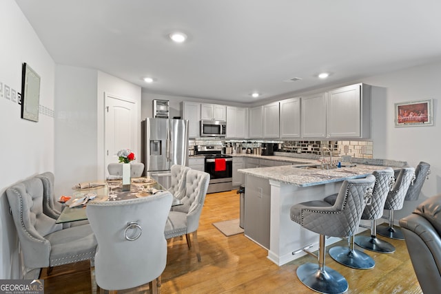 kitchen featuring a breakfast bar, light hardwood / wood-style floors, light stone counters, kitchen peninsula, and stainless steel appliances