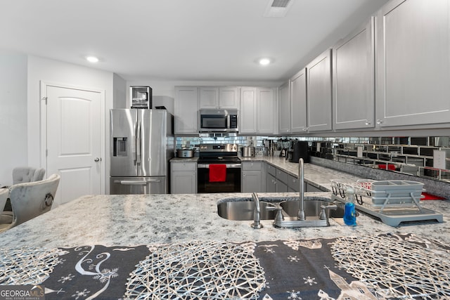 kitchen with appliances with stainless steel finishes, backsplash, light stone counters, and gray cabinetry