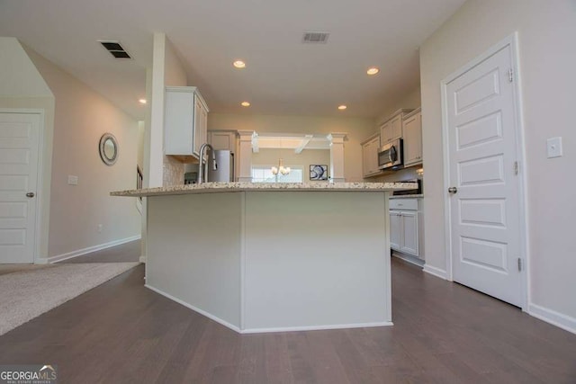 kitchen with kitchen peninsula, dark hardwood / wood-style floors, light stone countertops, appliances with stainless steel finishes, and white cabinetry