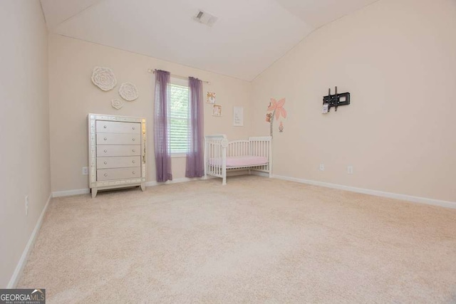 unfurnished bedroom featuring light carpet, vaulted ceiling, and a nursery area