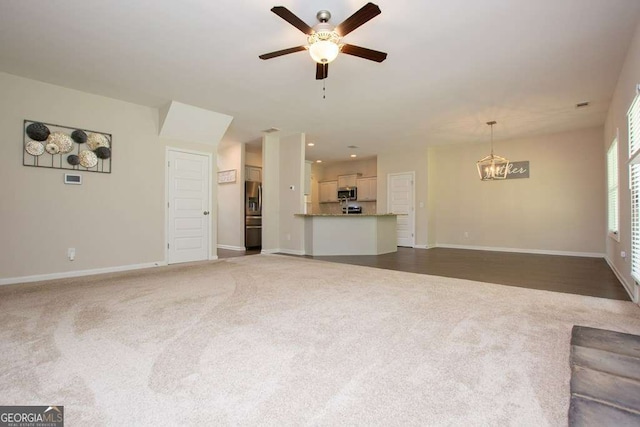 unfurnished living room with dark colored carpet and ceiling fan with notable chandelier