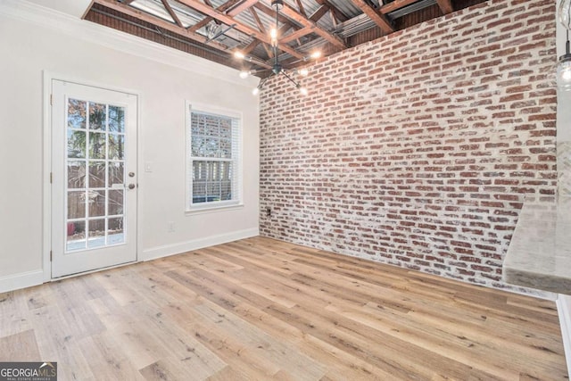 empty room with ornamental molding, light hardwood / wood-style flooring, brick wall, and an inviting chandelier