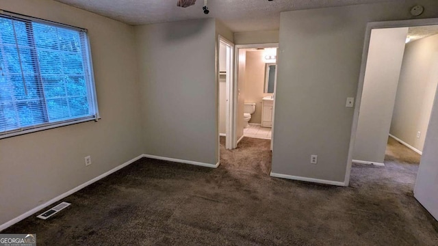 unfurnished bedroom featuring a textured ceiling, dark carpet, and connected bathroom