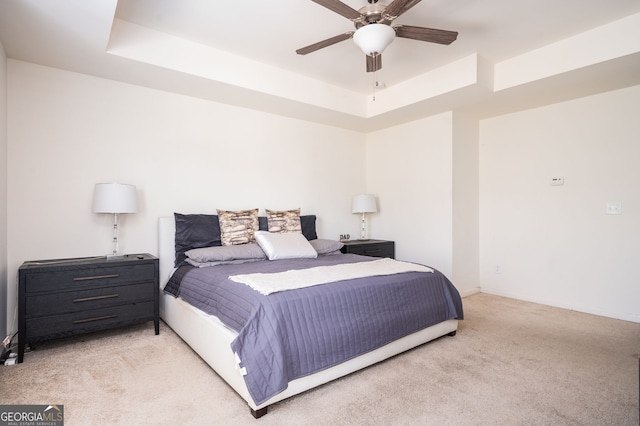 carpeted bedroom with ceiling fan and a tray ceiling