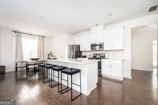 kitchen featuring a kitchen breakfast bar, white cabinetry, an island with sink, and appliances with stainless steel finishes