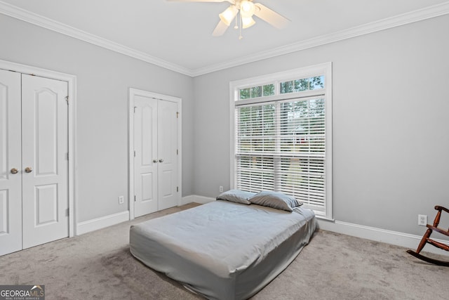 bedroom featuring ceiling fan, ornamental molding, light carpet, and two closets