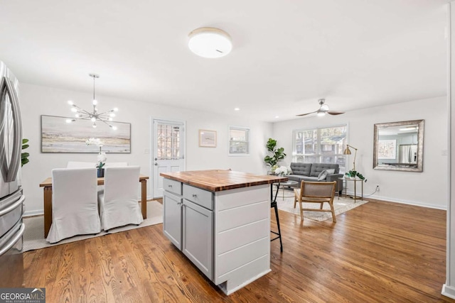 kitchen featuring a breakfast bar, ceiling fan with notable chandelier, pendant lighting, light hardwood / wood-style flooring, and a center island