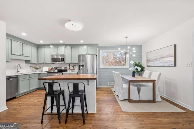 kitchen with appliances with stainless steel finishes, light wood-type flooring, tasteful backsplash, pendant lighting, and a breakfast bar area