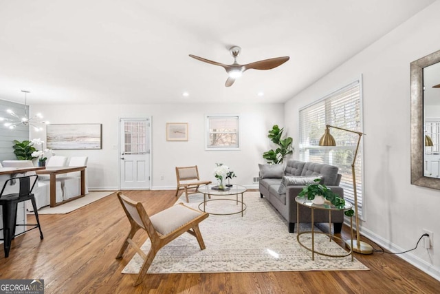 living room with ceiling fan with notable chandelier and light hardwood / wood-style flooring