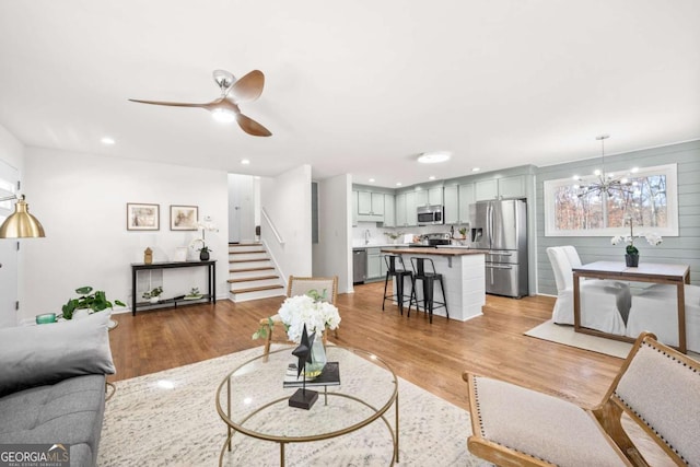 living room with ceiling fan with notable chandelier and light wood-type flooring