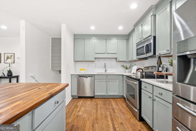 kitchen with decorative backsplash, wood counters, stainless steel appliances, sink, and light hardwood / wood-style flooring